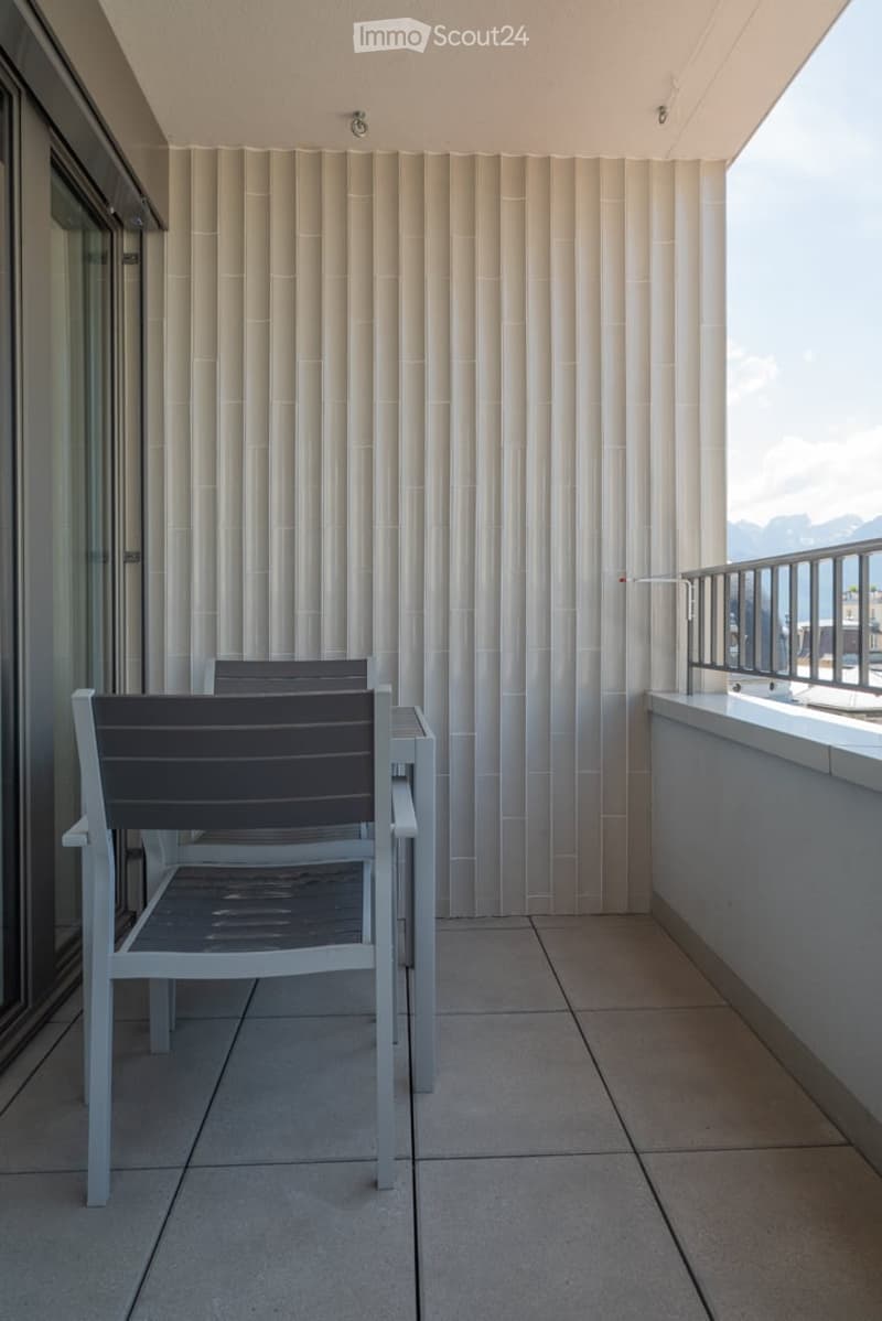 Balcony with modern white chairs and a small table, featuring a textured white wall and a metal railing.