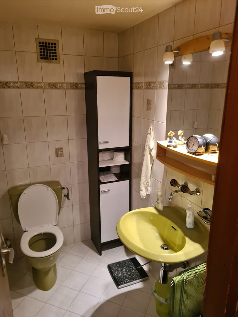 Bathroom with a green toilet, a yellow sink, a mirror, a cabinet, and a towel hanging on the wall.