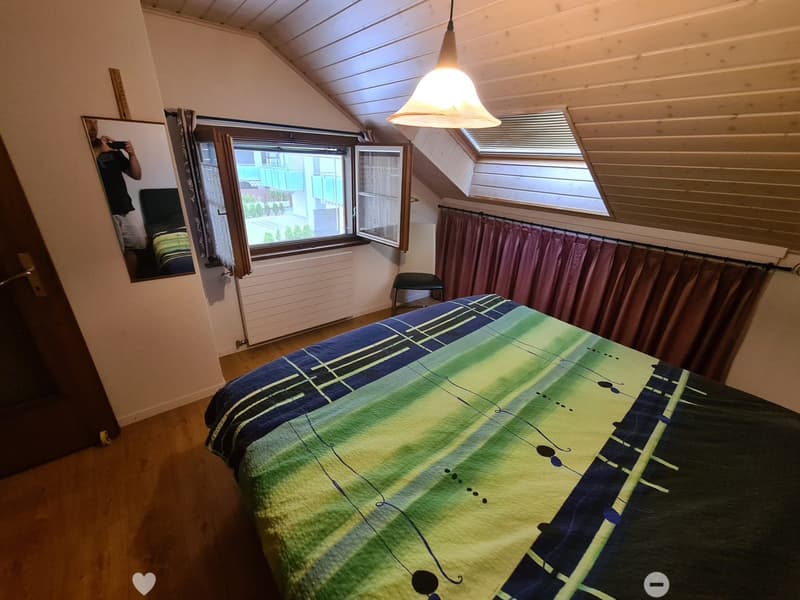Cozy attic bedroom with wooden floors, slanted ceilings, large windows, and a colorful bedspread.