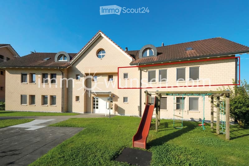 Two-story house with beige brick facade, multiple windows, and a well-maintained lawn with a playground featuring a slide and climbing frame.