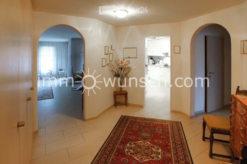 Bright hallway with tiled flooring, arched doorways leading to adjacent rooms, small wooden side table with vase, and framed pictures on the wall.