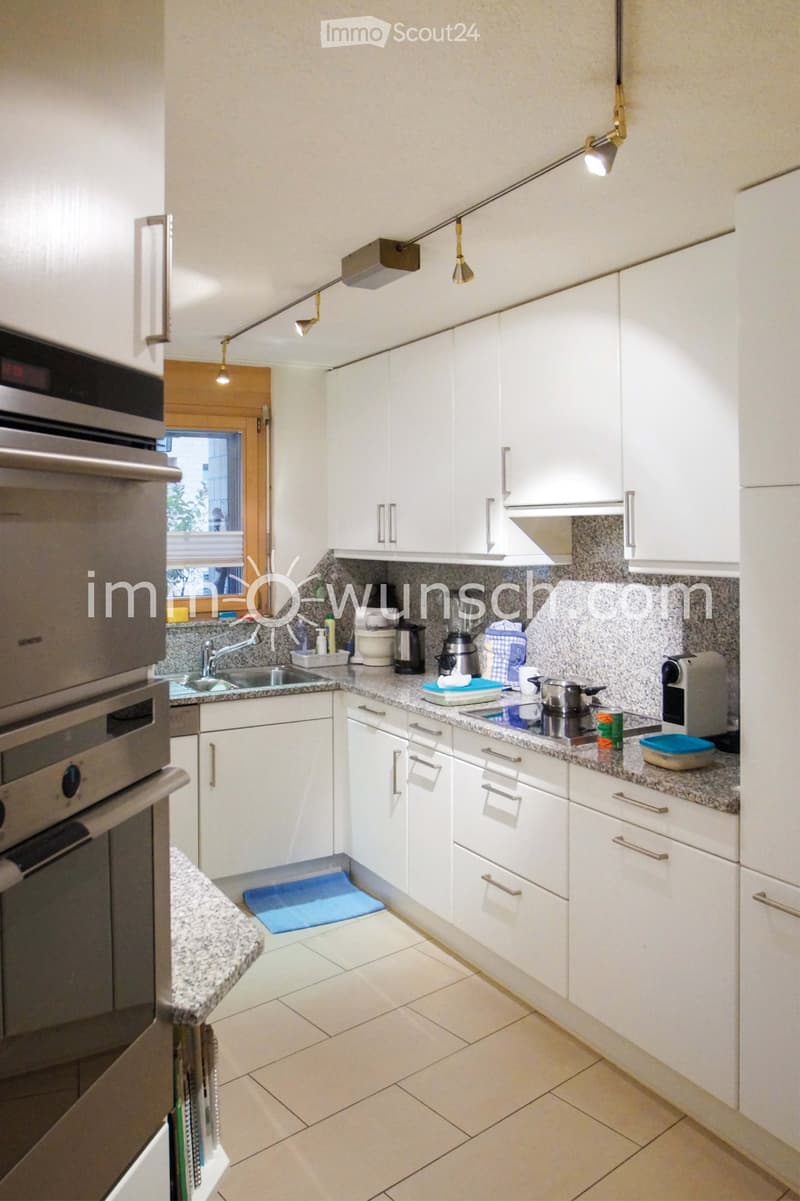 Modern kitchen with white cabinets, granite countertops, stainless steel appliances, and various kitchen items on the counter.