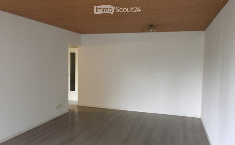 An empty room with wooden floor, white walls and ceiling, open door, and electrical outlets.