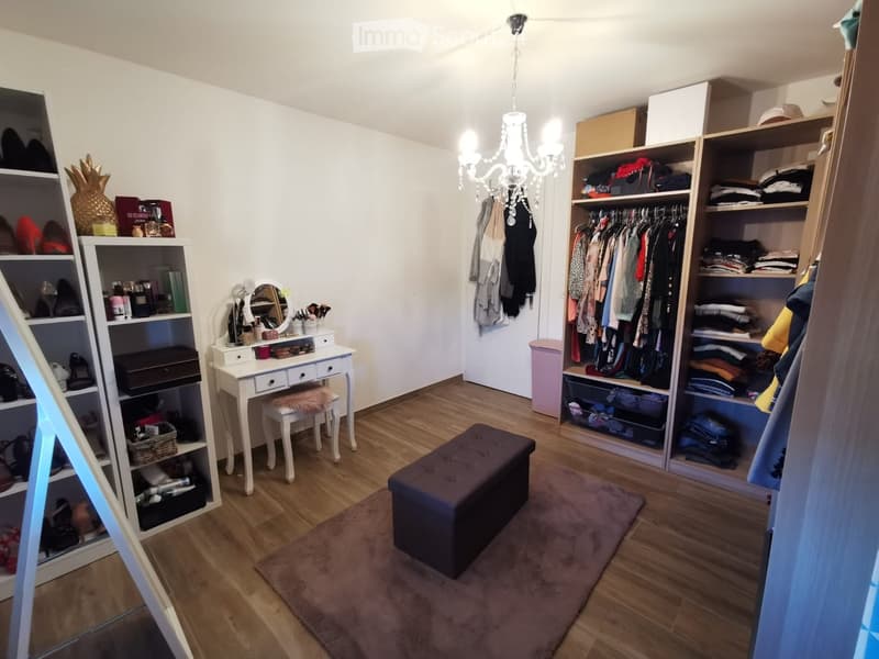 Well-organized walk-in closet with wooden flooring, large built-in wardrobe, vanity table with mirror, and various storage shelves.