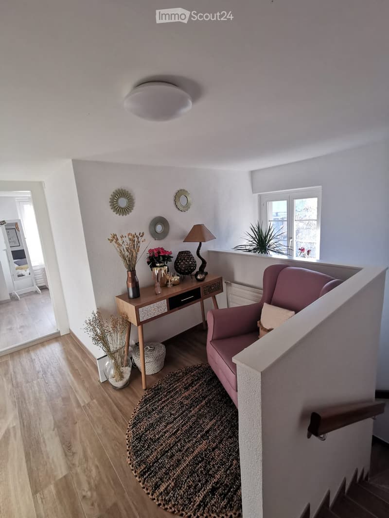 A modern, well-lit hallway with a pink sofa, wooden table, decorative vases, and a round rug on the floor.