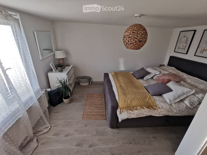 Cozy bedroom with a large bed, nightstand, lamp, mirror, and decorative items.