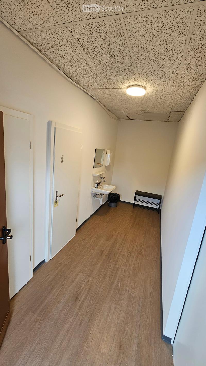 Empty hallway with wooden flooring, white walls, and a small sink area visible at the end.