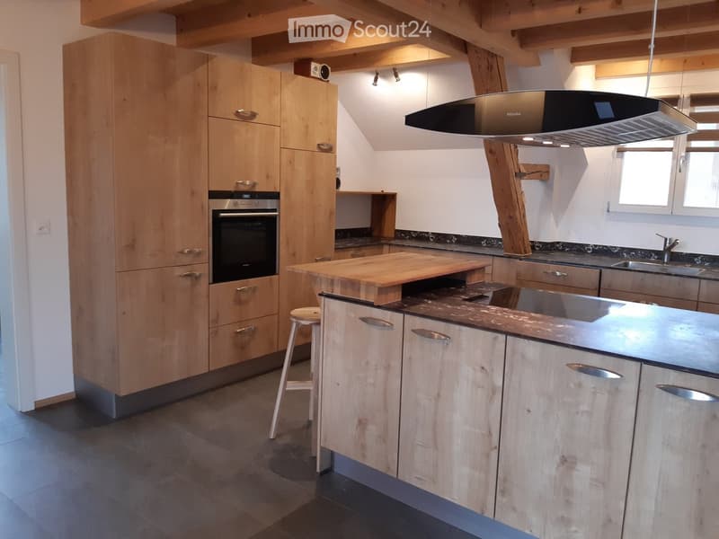 Modern kitchen with light wooden cabinets, stainless steel appliances, island with wooden countertop, and a single stool.