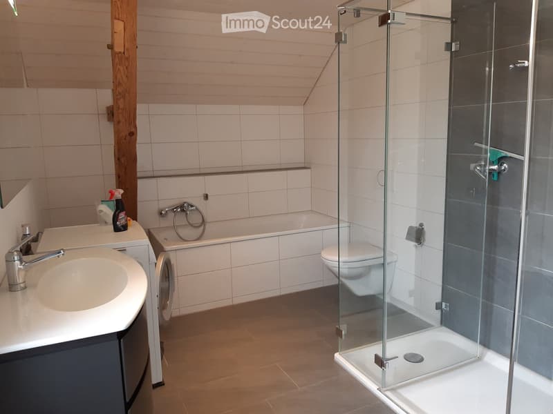 Modern bathroom with a white sink, bathtub, toilet, and glass-enclosed shower. Features wooden flooring and white tiled walls.
