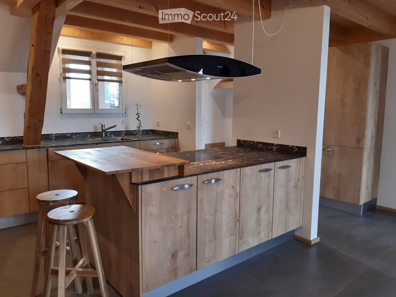 Modern kitchen with wooden island, two wooden stools, sink, faucet, cabinets, and a range hood. Exposed wooden beams on the ceiling.