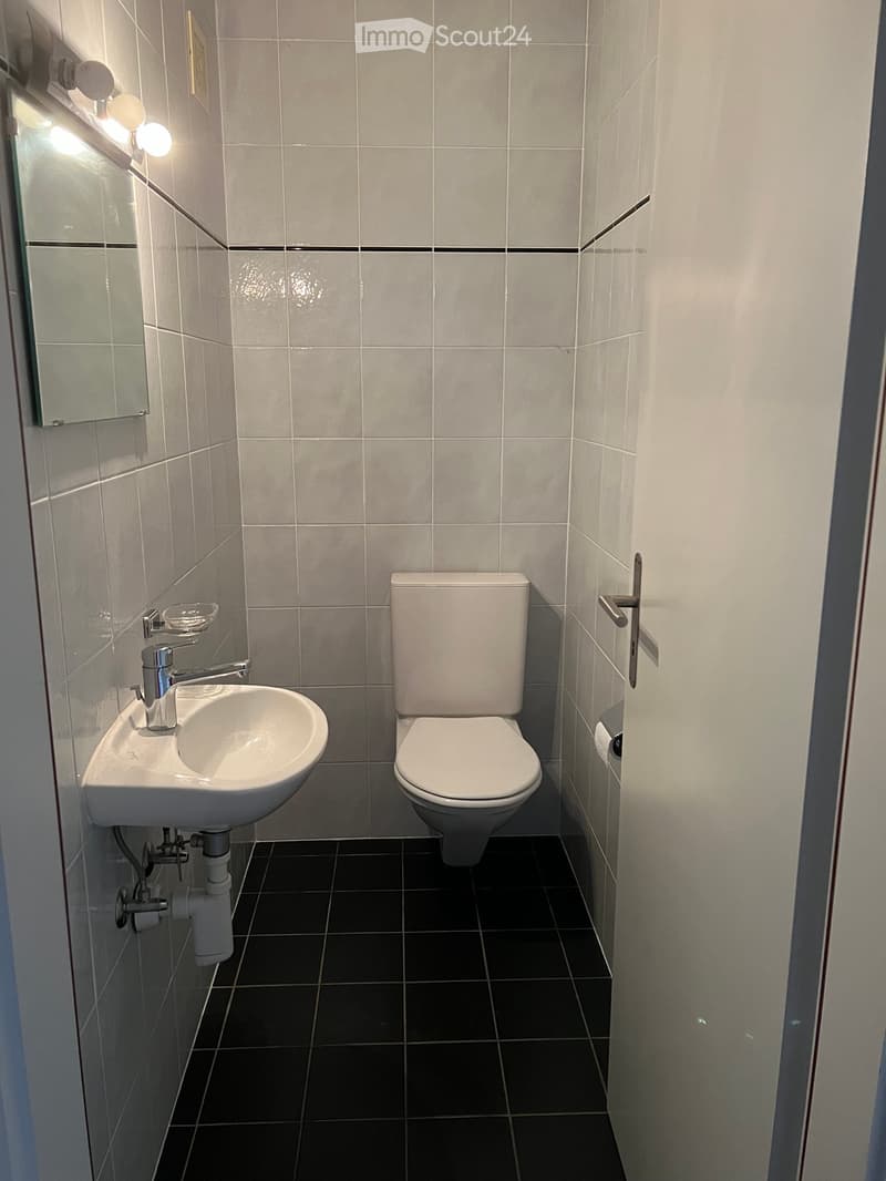 Modern bathroom with white tiles, a white sink, chrome faucet, toilet, and a mirror with built-in lighting.