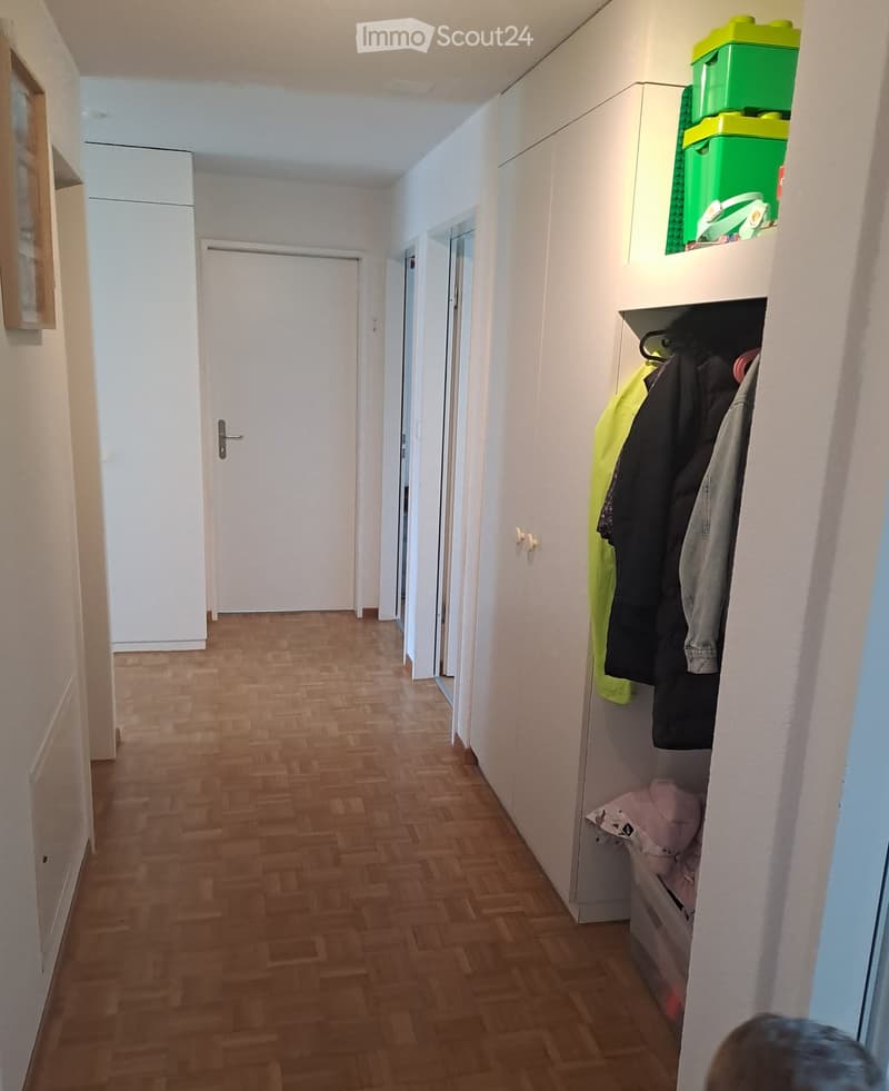 Wooden floor, white walls, white doors, closet with clothes, green storage boxes on top of the closet
