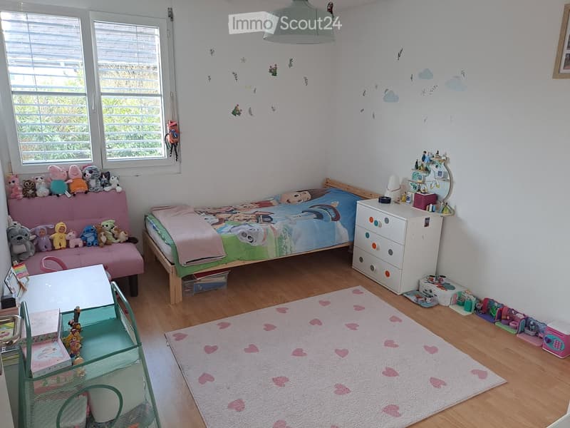 A child's bedroom with a bed, toys, a pink chair, a white cabinet, and a rug