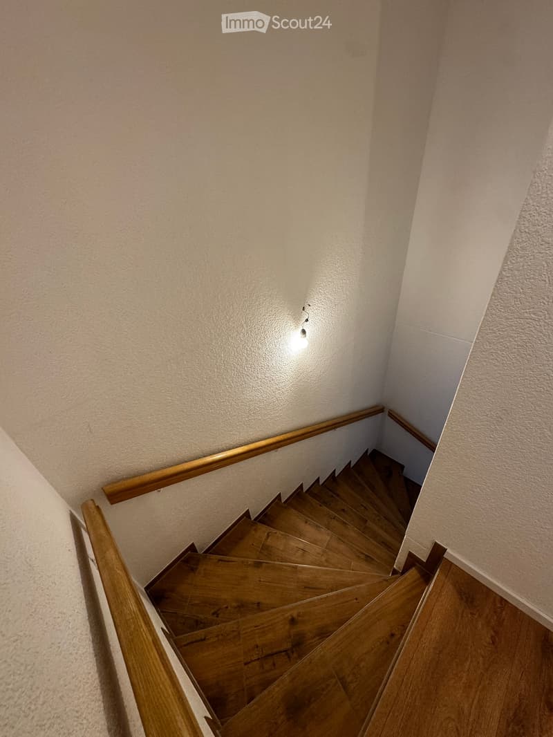 Wooden staircase with wooden handrails and a single light fixture on the wall.