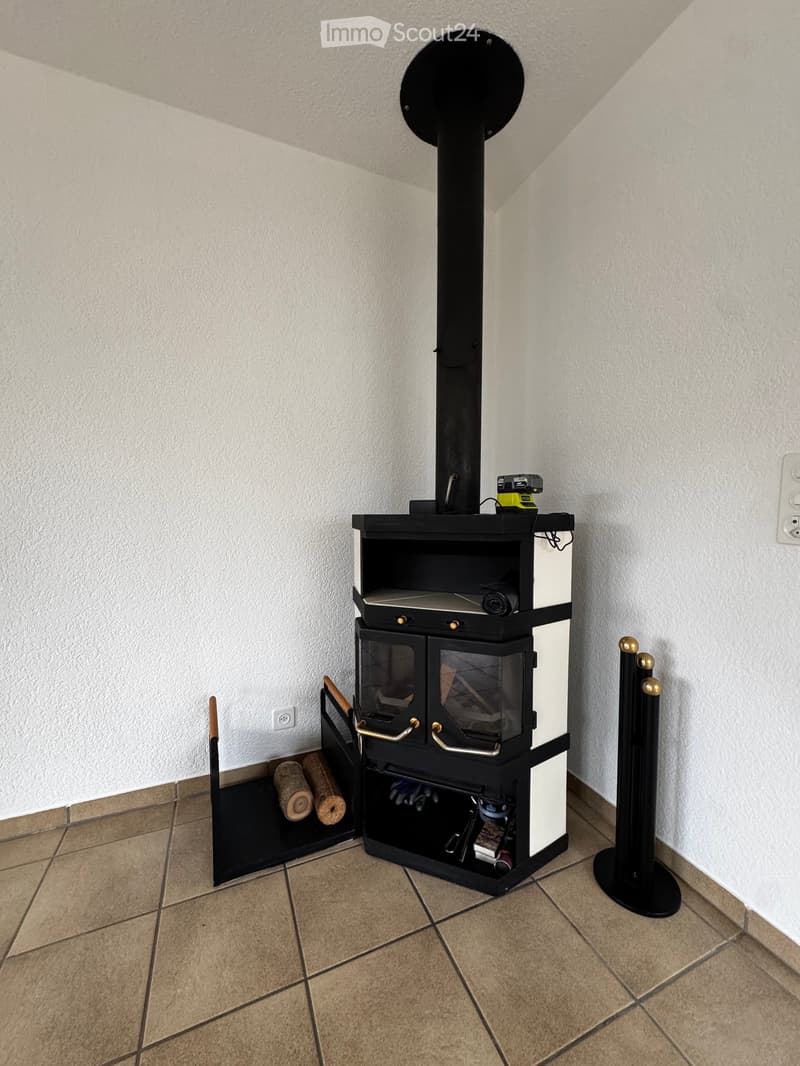 Corner room with a modern black wood-burning stove, storage compartments, and wood logs nearby.