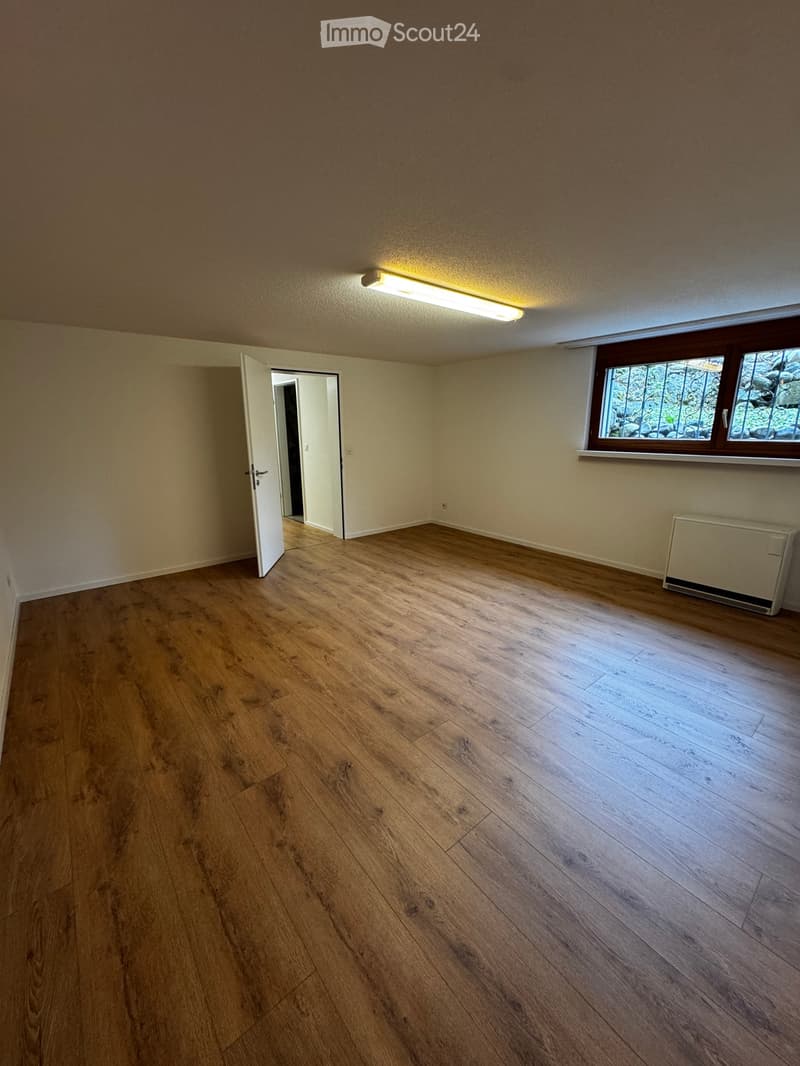 Empty room with wooden flooring, white walls, a window with decorative bars, and a radiator on the wall.