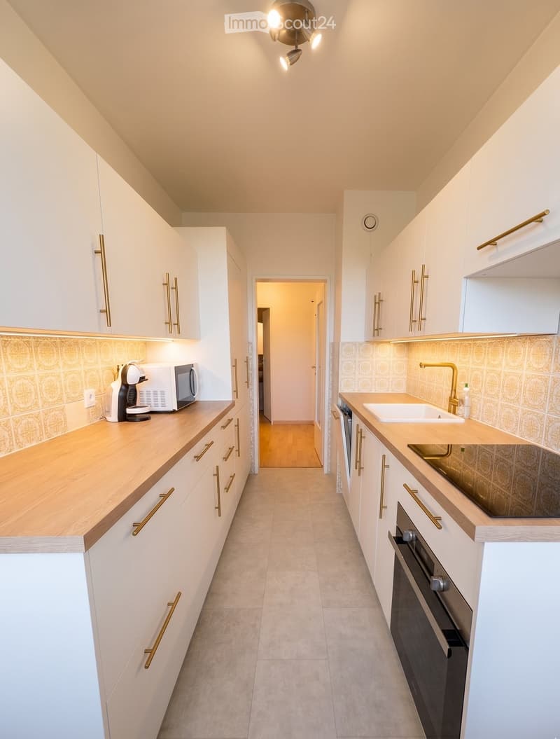 Modern kitchen with white cabinets, wooden countertops, and gold handles. Features a sink, faucet, oven, microwave, and coffee machine.