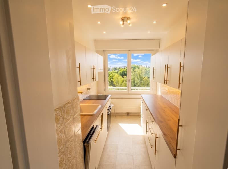 Modern kitchen with white cabinets, wooden countertops, a sink, bathtub, and a dishwasher. Large windows offer a view of greenery outside.