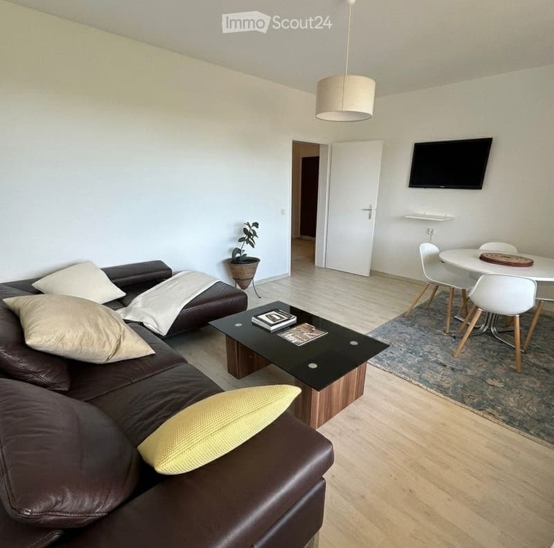 Modern living and dining area with a brown leather sofa, coffee table, dining table with chairs, and a television mounted on the wall.