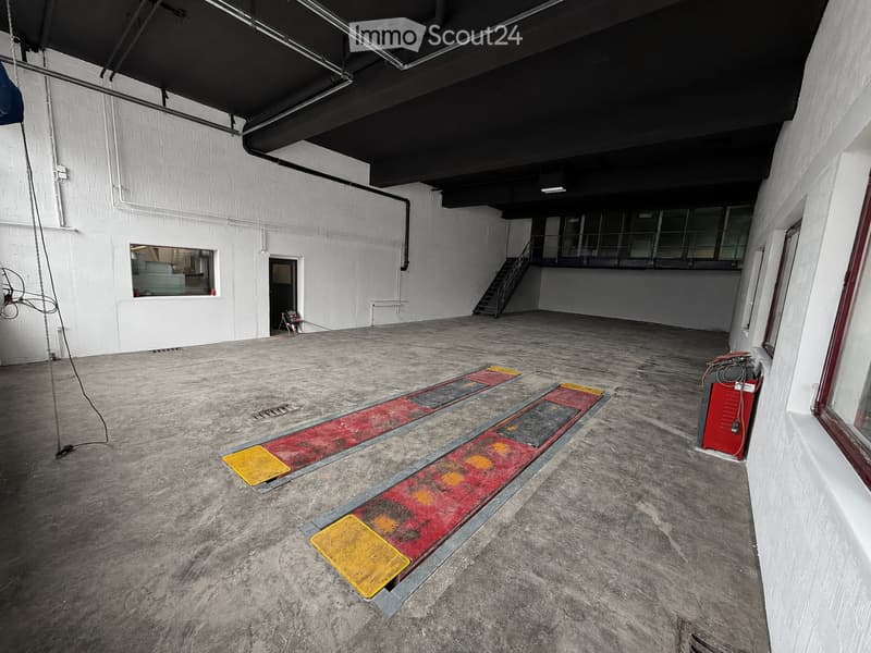 Empty industrial-style room with concrete floor, white brick walls, metal staircase leading to an upper level, and several marked loading ramps on the floor.