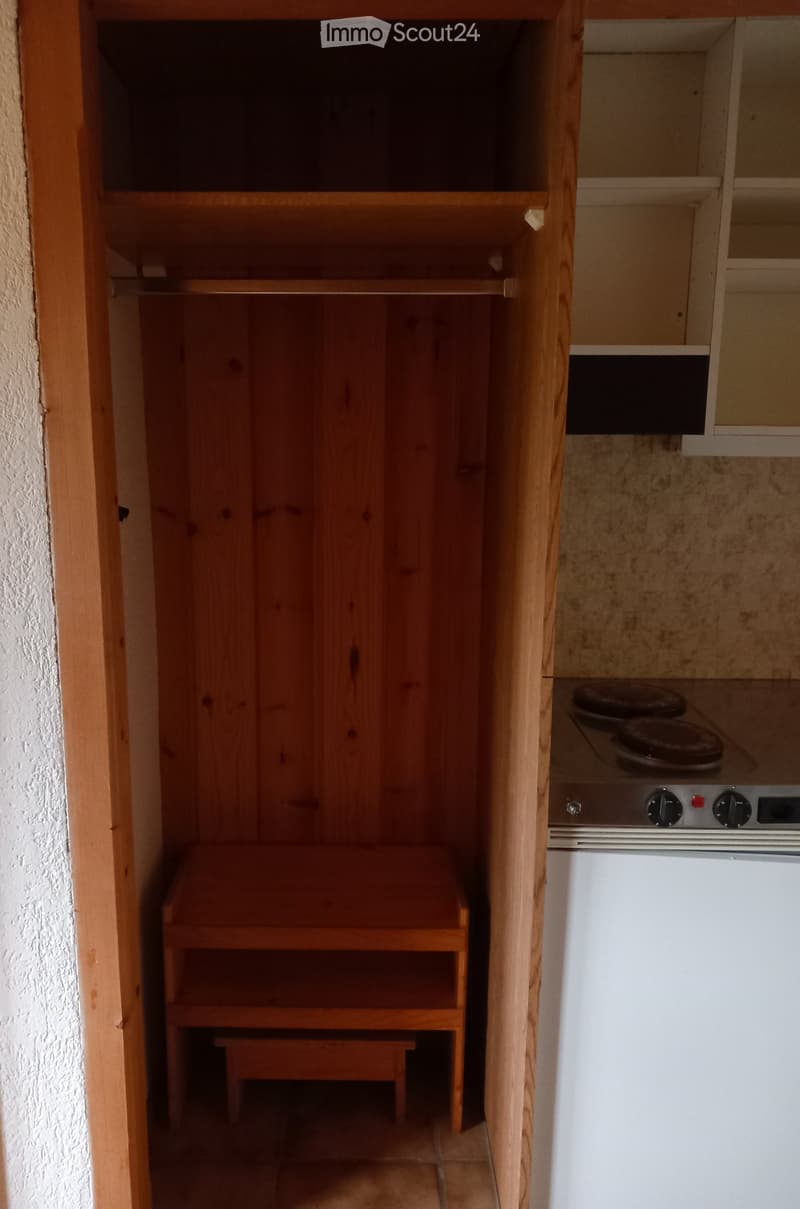 A small kitchen area with a wooden cabinet, a refrigerator, and a stove with four burners.