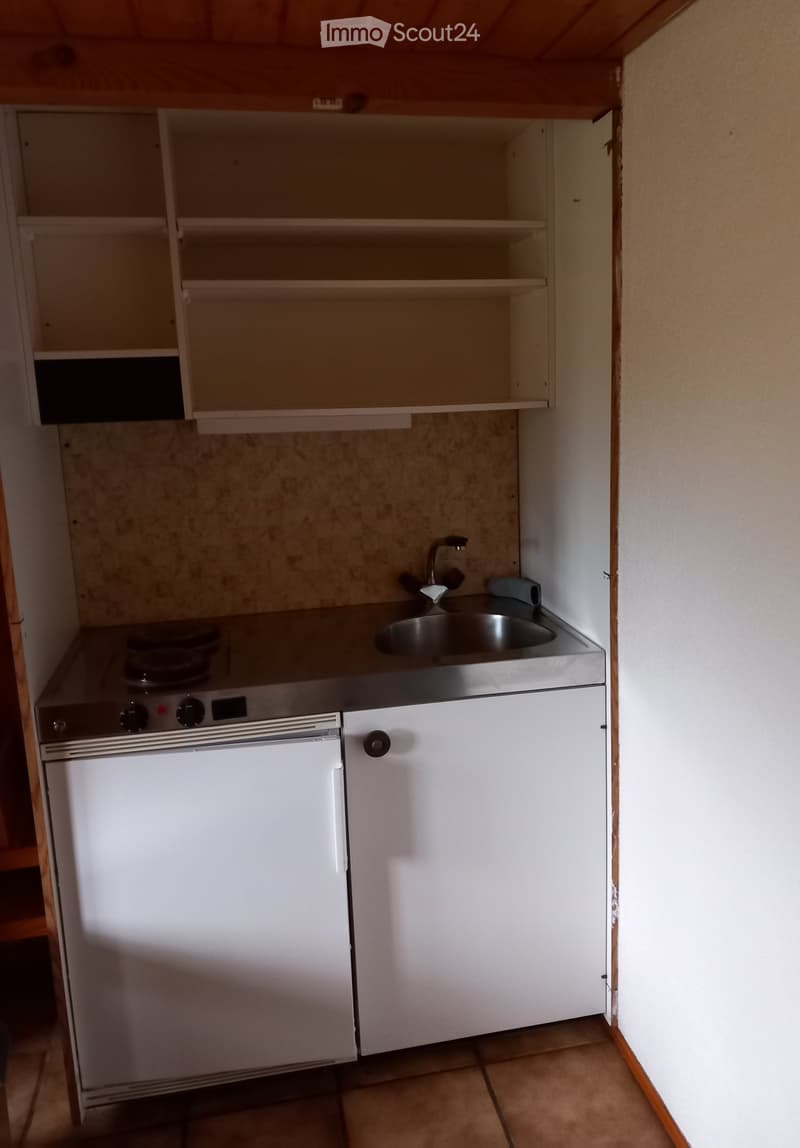 Compact kitchen with a refrigerator, oven, sink, faucet, and cabinet. The space is small and functional, with tiled flooring and wooden ceiling.