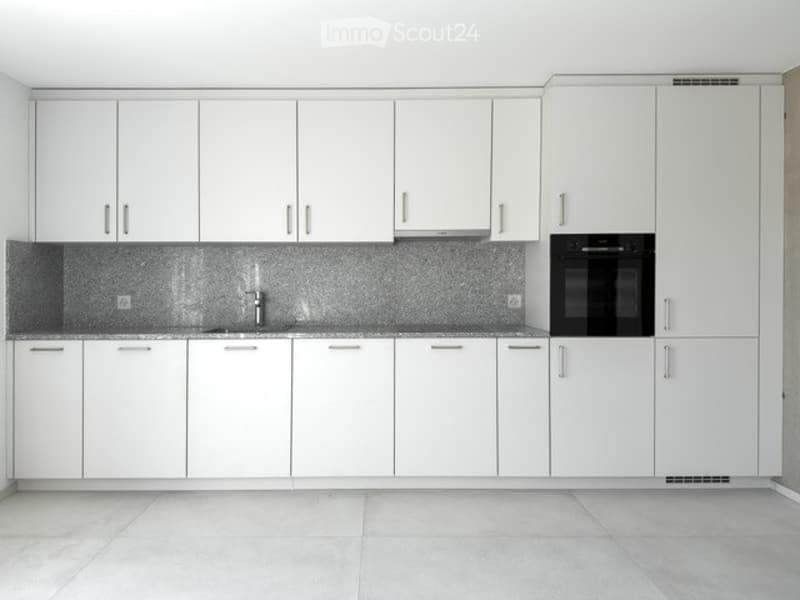 Modern kitchen with white cabinets, a stainless steel sink, and a built-in oven. The countertops are tiled, and the floor is tiled as well.