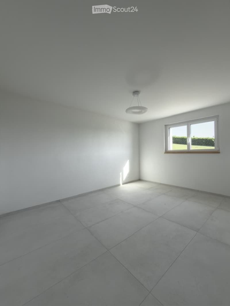 Empty room with white walls, tiled floor, and a single window with white frame. A ceiling light fixture is visible.