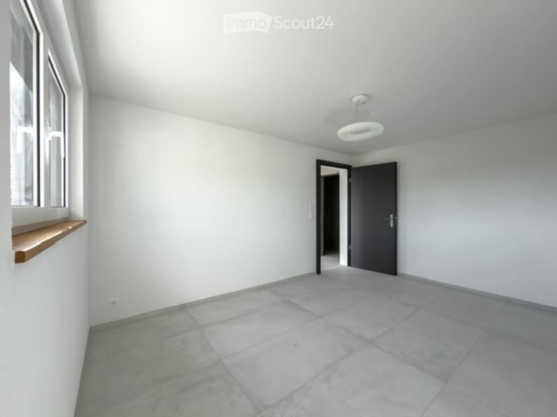Empty room with white walls, tiled floor, large window, and a single door leading to another space.