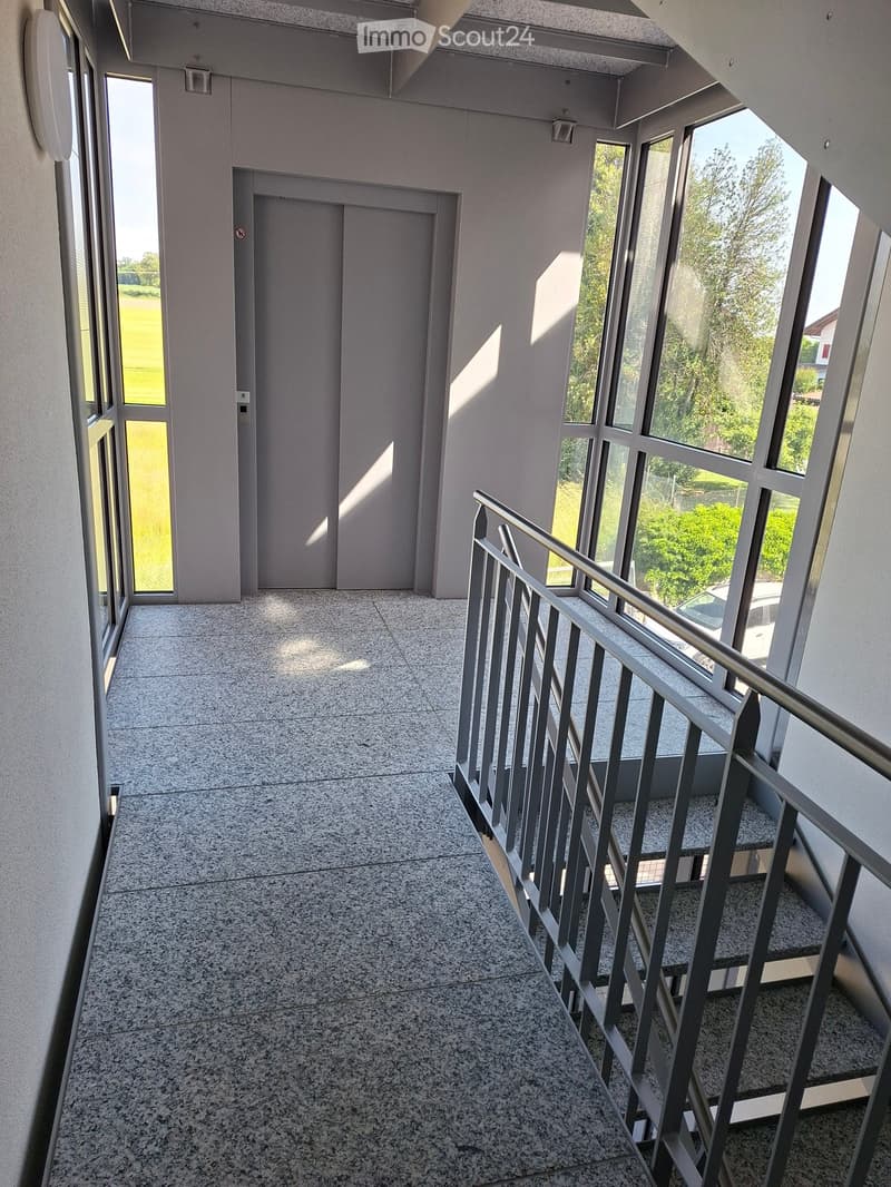 Modern hallway with polished granite flooring, large windows, and a staircase with metal railing leading upwards.