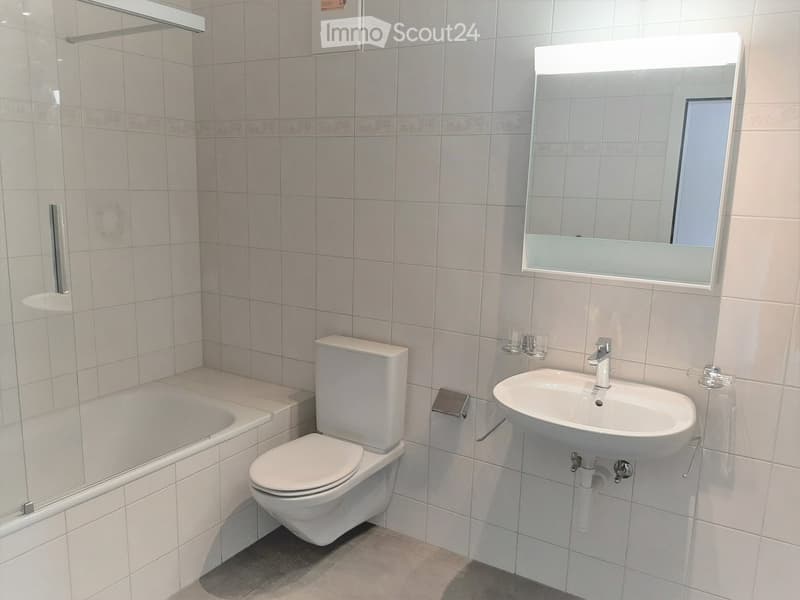 Modern bathroom with white tiles, a toilet, a sink with a mirror, and a bathtub.