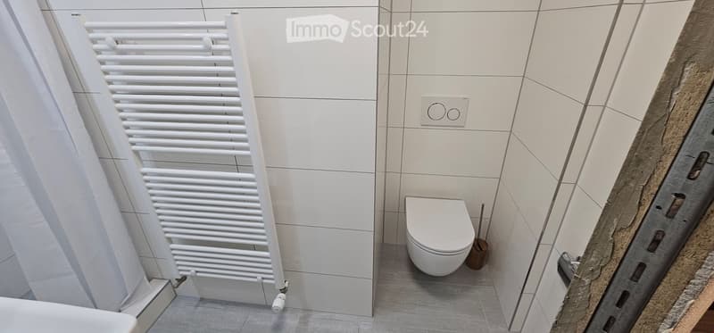 Modern bathroom with white tiled walls, a toilet, a white radiator, and a toilet brush holder.