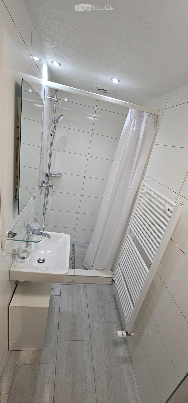 Modern bathroom with white tiles, a glass shower enclosure, a white radiator, and a sink with a mirror above it.