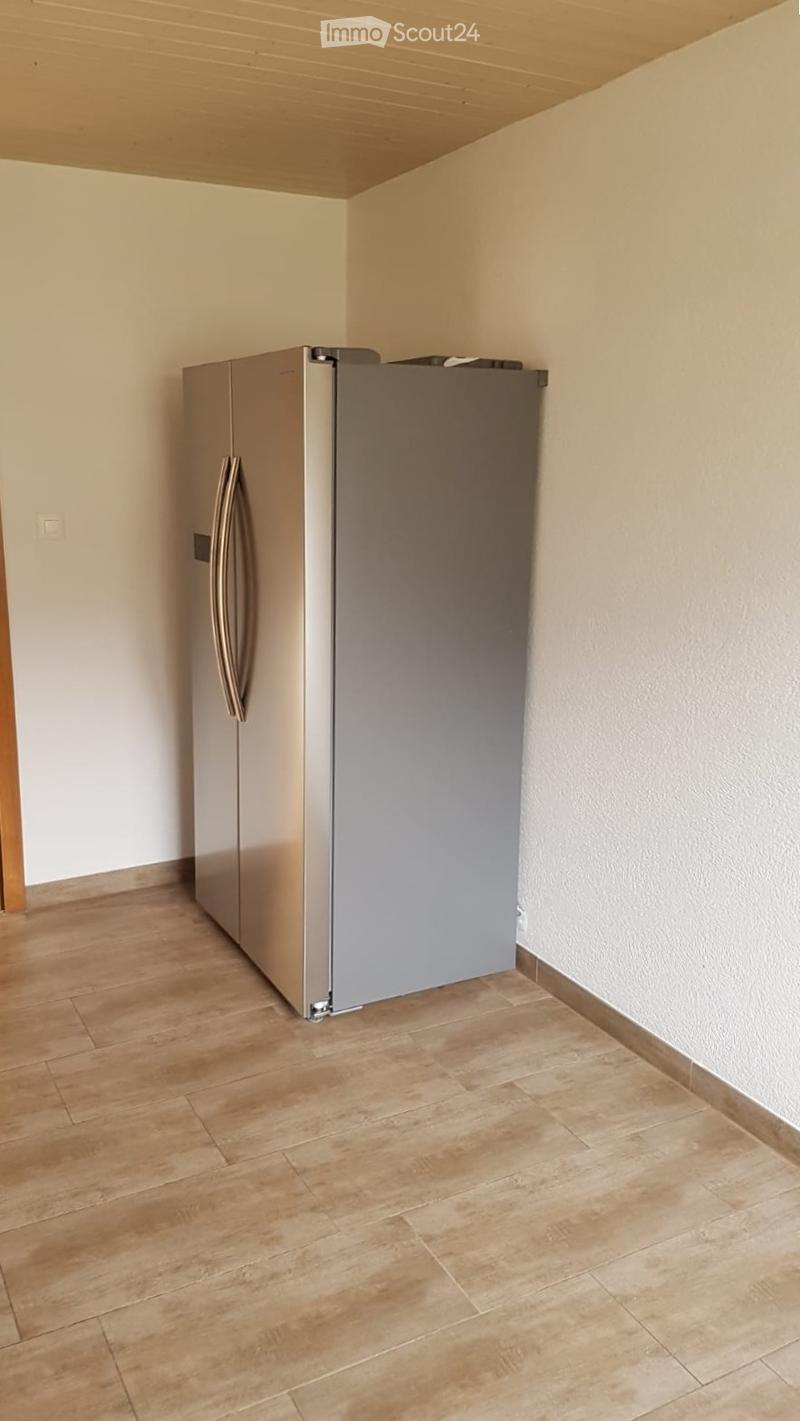 Empty room with light-colored walls, wooden flooring, and a stainless steel refrigerator placed against one wall.