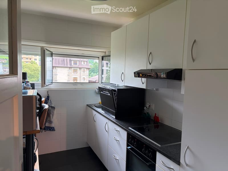 Modern kitchen with white cabinets, stainless steel appliances, and a large window overlooking a cityscape.