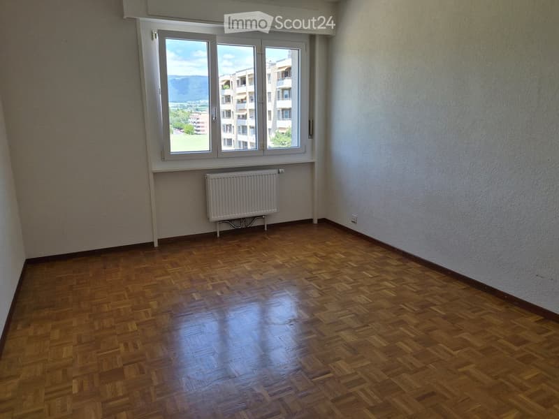 Empty room with wooden flooring, white walls, and a large window offering a view of the outside. A radiator is placed below the window.