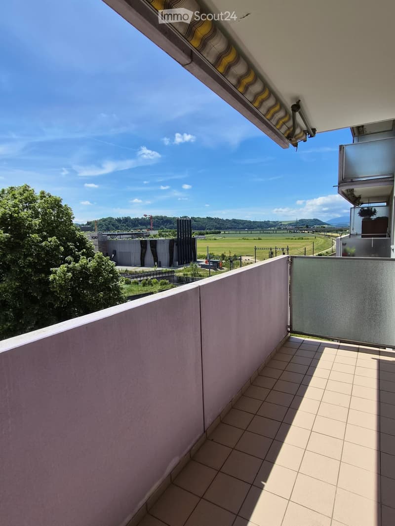 Balcony with tiled floor, low concrete railing, and a view of a green landscape and distant buildings.