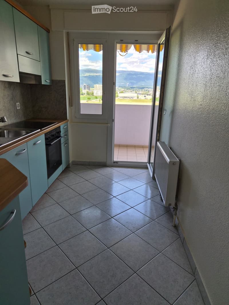 Empty kitchen with tiled floor, light blue cabinets, and a window opening to a balcony with a scenic view.