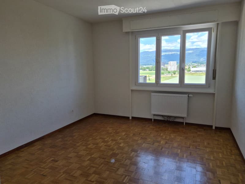 Empty room with wooden flooring, white walls, and large windows offering a scenic view of the landscape.