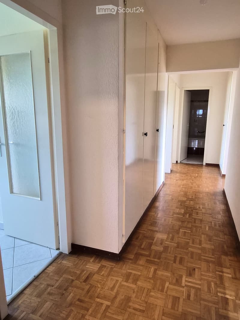 Empty hallway with wooden herringbone flooring, white walls, and multiple doors leading to other rooms.