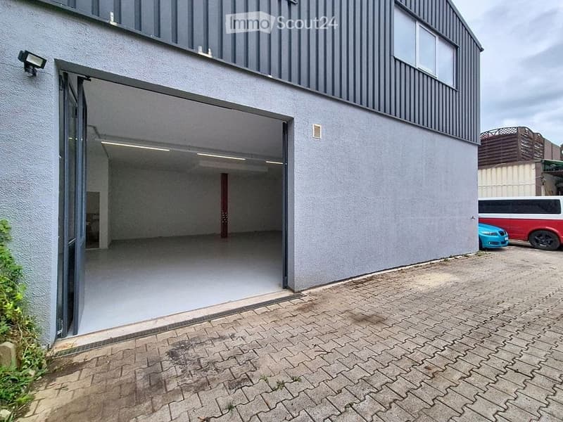 Modern industrial-style building with a large open garage entrance, grey exterior walls, and a paved driveway.