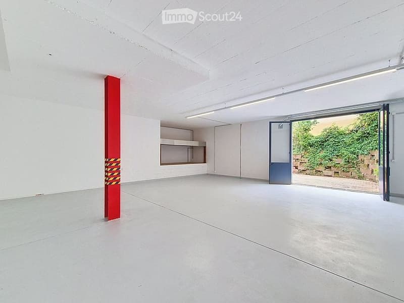 Empty room with white walls, concrete floor, and a large sliding door leading to an outdoor area. A red column and a small built-in shelf are visible.