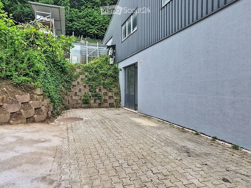 Modern building with grey exterior, raised ground floor, brick pathway, and greenery on the slope.