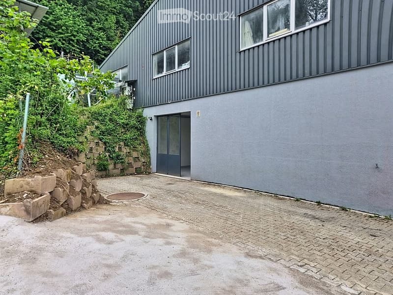 Modern two-story building with grey exterior, raised ground floor, and a paved driveway.