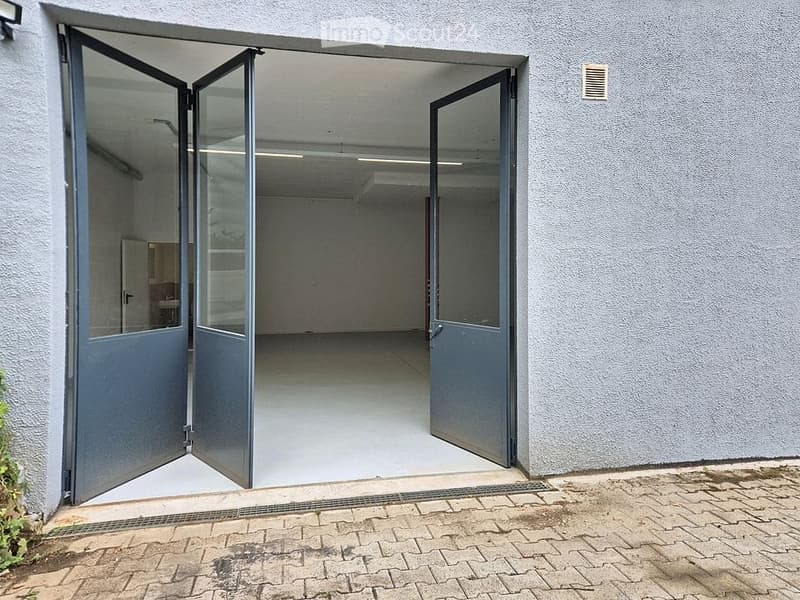 An empty room with grey walls and a white floor, viewed through a set of open sliding doors. The room has a simple, clean design with no visible furniture or equipment.