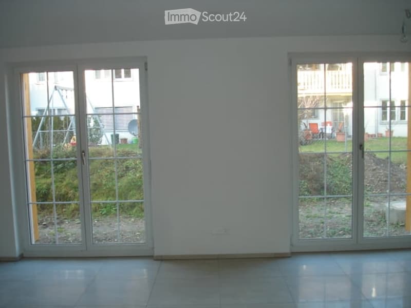 Empty room with large sliding glass doors leading to a garden area, tiled floor, and white walls.