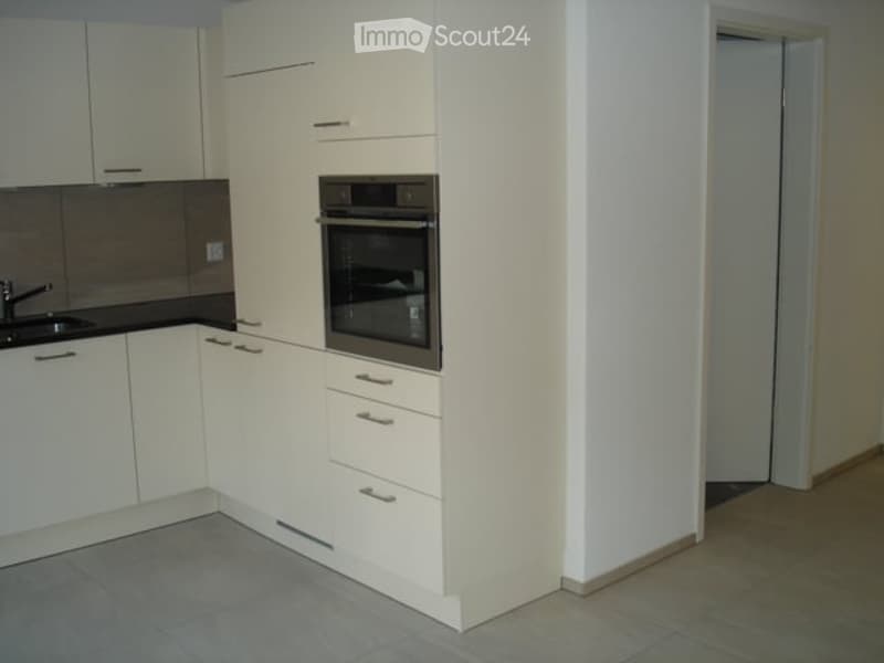 Modern kitchen with white cabinets, a built-in oven, and a sink. The space is clean and well-lit with tiled flooring.