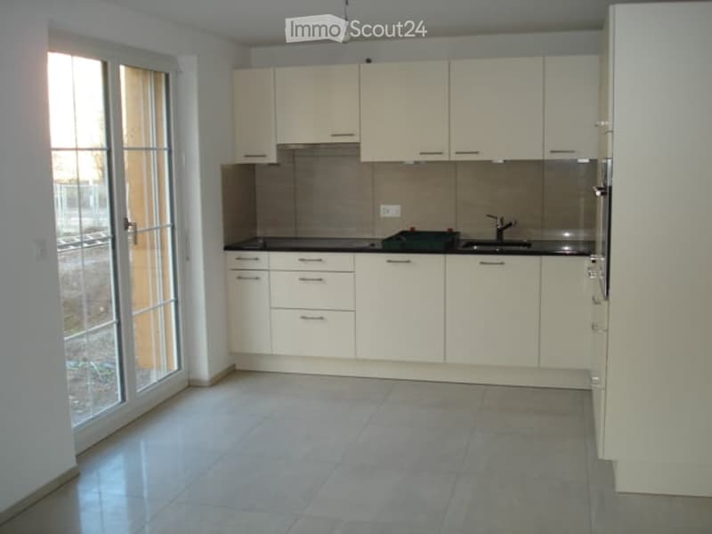 Empty kitchen with white cabinets, stainless steel appliances, and tiled flooring. Large window with glass door provides natural light.