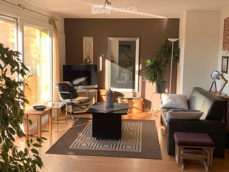Modern living room with a dark brown accent wall, large window, and a mix of contemporary and rustic furniture including a sofa, coffee table, and a chair.