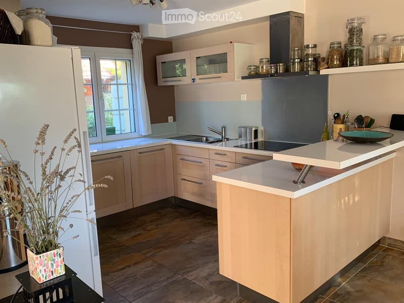Modern kitchen with light wood cabinets, stainless steel appliances, a central island, and a window overlooking the garden.
